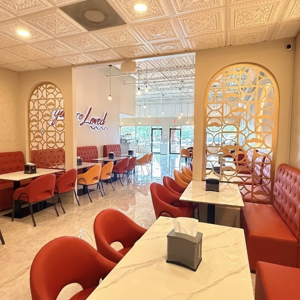 Warmly lit restaurant dining room with red and orange upholstered seating, marble tables, decorative screens, and a glowing wall accent.