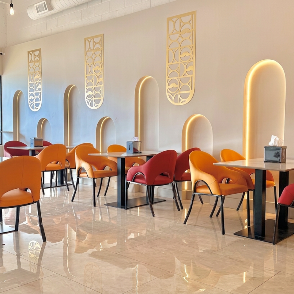 Bright modern restaurant dining room with colorful orange and red chairs, marble floors, decorative wall panels, and large windows.